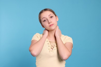 Photo of Teenage girl suffering from pain in neck on light blue background. Arthritis symptom