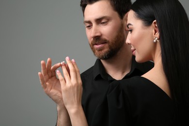 Photo of Man putting elegant ring on woman's finger against dark grey background, closeup