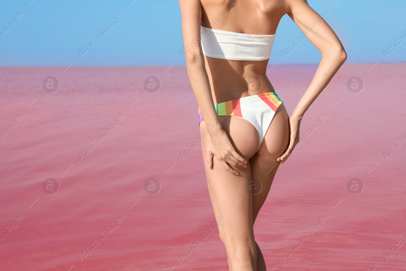 Photo of Beautiful woman in swimsuit posing near pink lake on sunny day, closeup