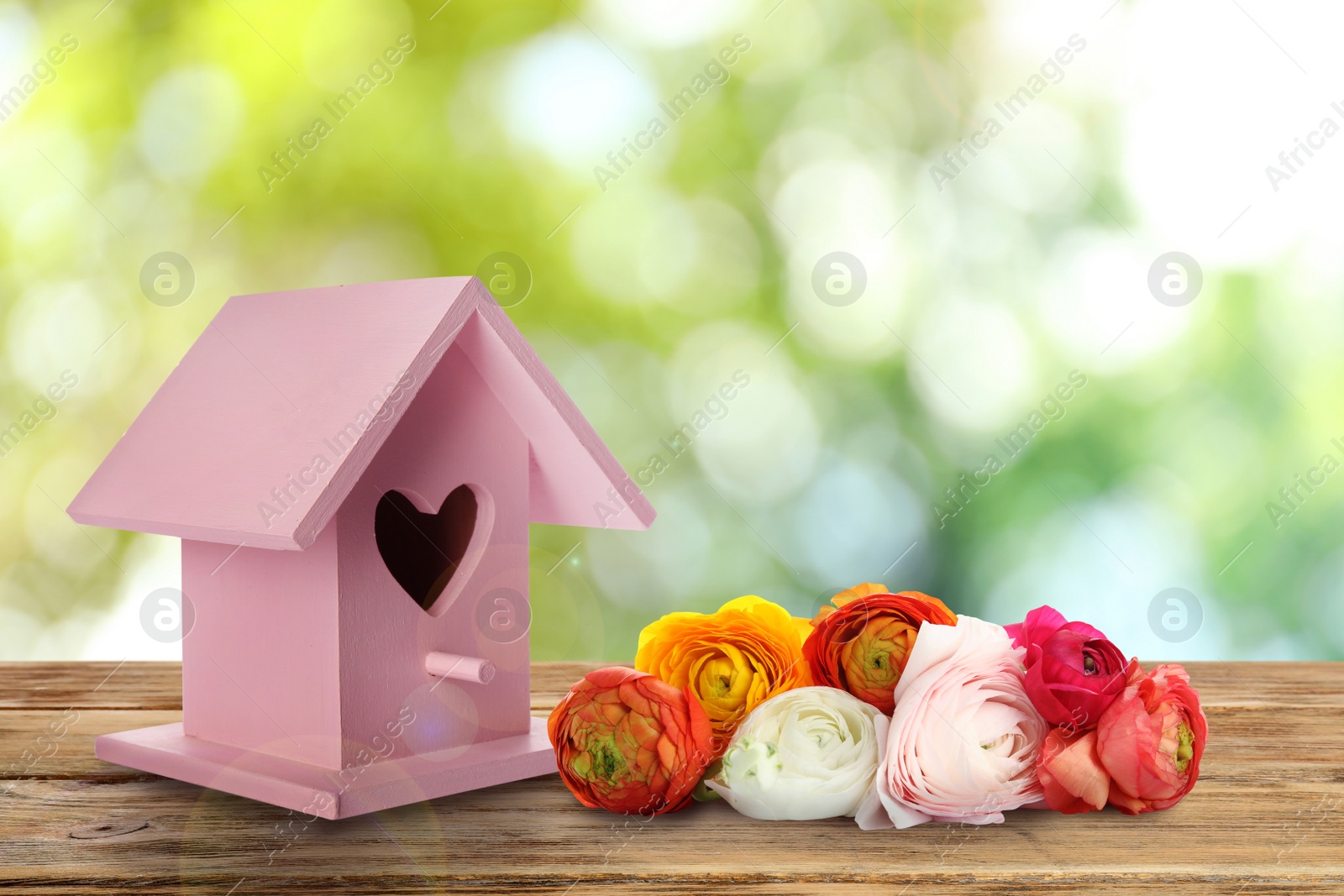 Image of Beautiful bird house and spring flowers on wooden table outdoors