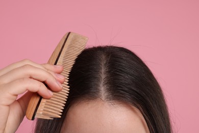 Woman with comb examining her hair and scalp on pink background, closeup