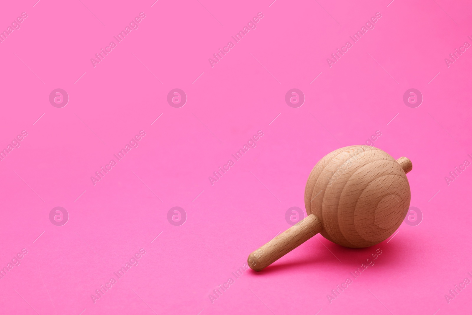 Photo of One wooden spinning top on pink background, space for text. Toy whirligig