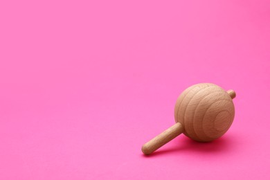 One wooden spinning top on pink background, space for text. Toy whirligig