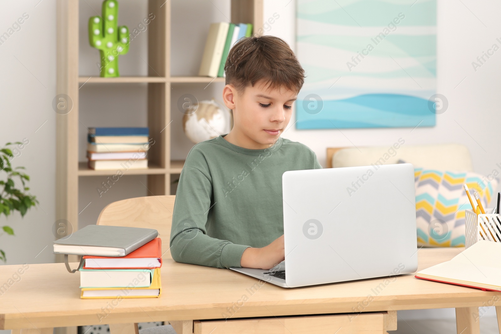 Photo of Boy using laptop at desk in room. Home workplace