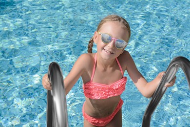 Photo of Cute little girl with sunglasses on ladder in swimming pool