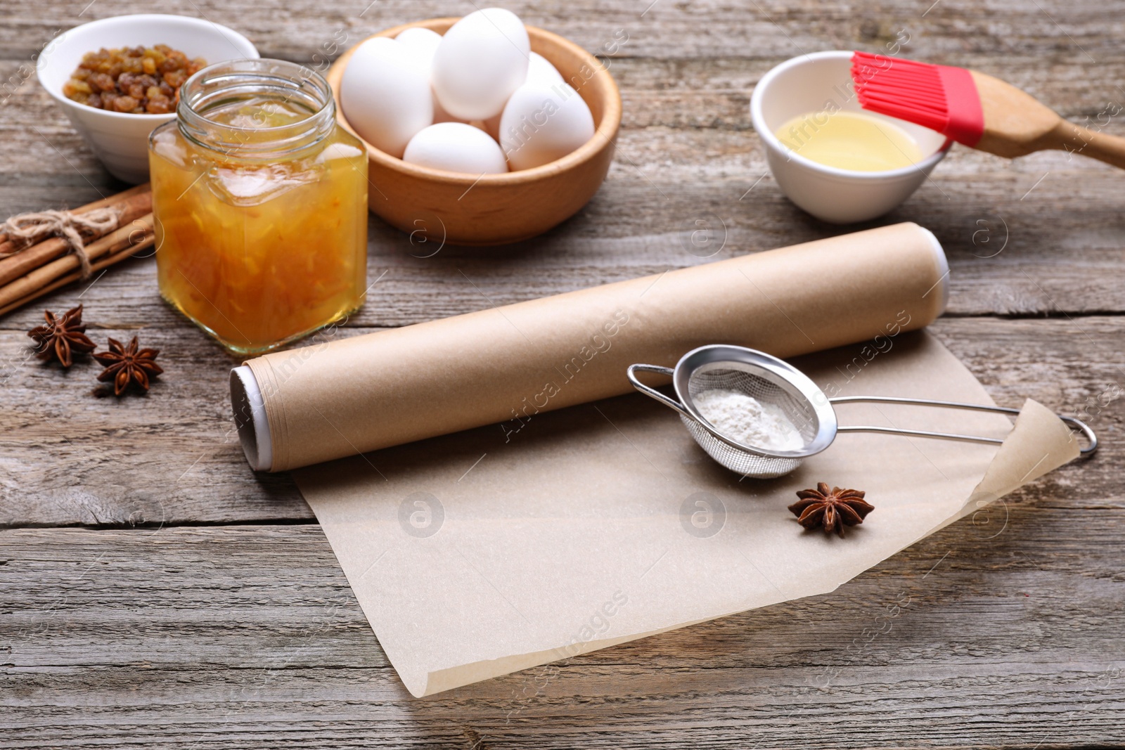 Photo of Roll of baking parchment paper, different ingredients and kitchen tools on wooden table