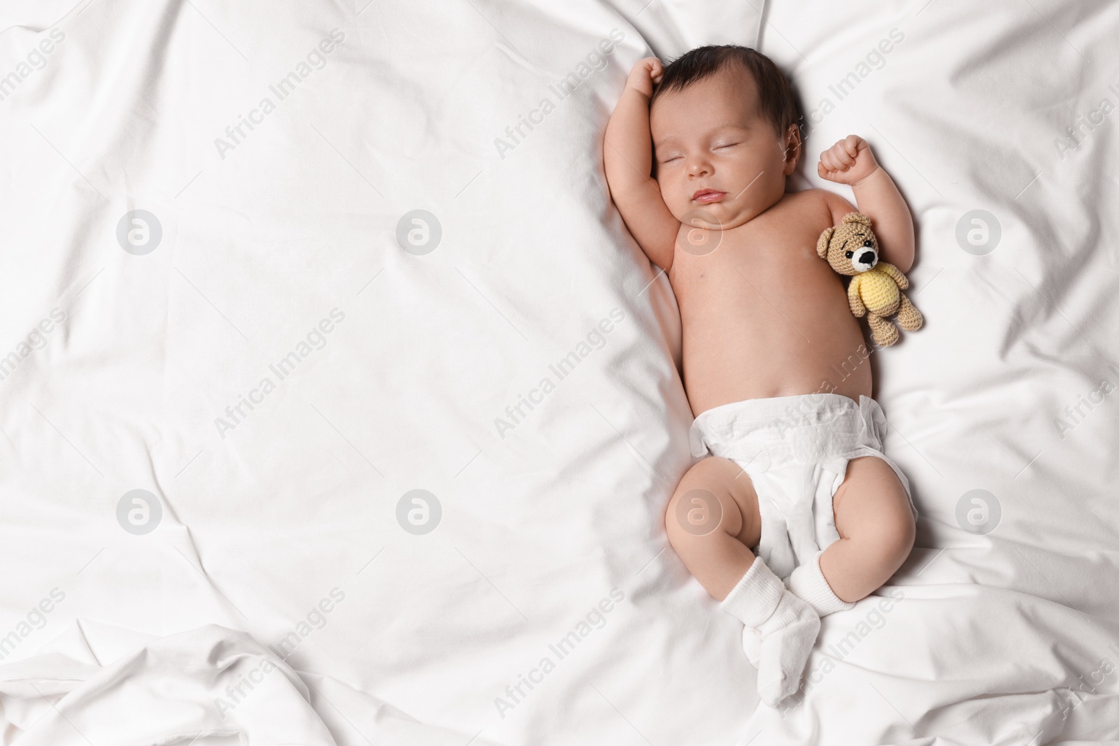 Photo of Cute little baby with toy bear sleeping on soft bed, top view. Space for text