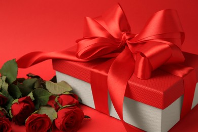 Beautiful gift box with bow and roses on red background, closeup