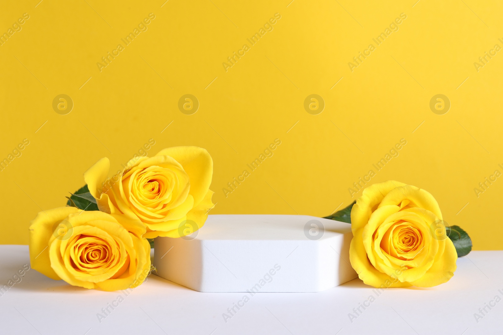 Photo of Beautiful presentation for product. Podium and roses on white table against yellow background, space for text