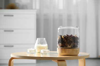 Decorative jar with aromatic potpourri and candles on wooden table in room, space for text