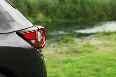 Photo of New black modern car near river, closeup of taillight. Space for text