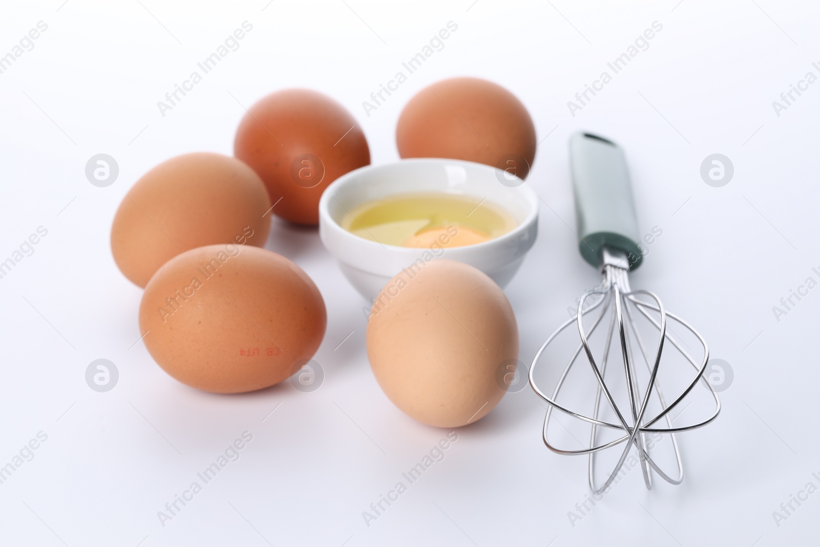 Photo of Whisk, whole and broken eggs isolated on white