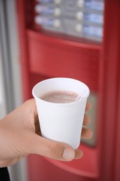 Photo of Woman holding paper cup with coffee near vending machine, closeup