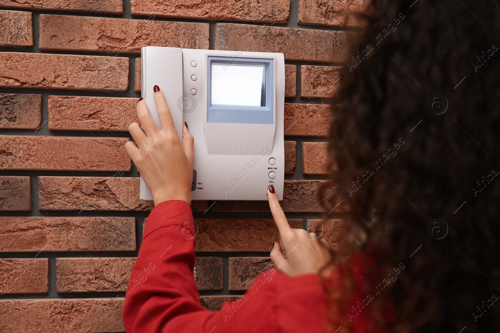 Photo of African-American woman pressing button on intercom panel indoors