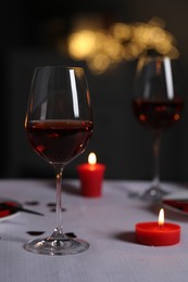 Photo of Romantic table setting with glasses of red wine and burning candles against blurred lights