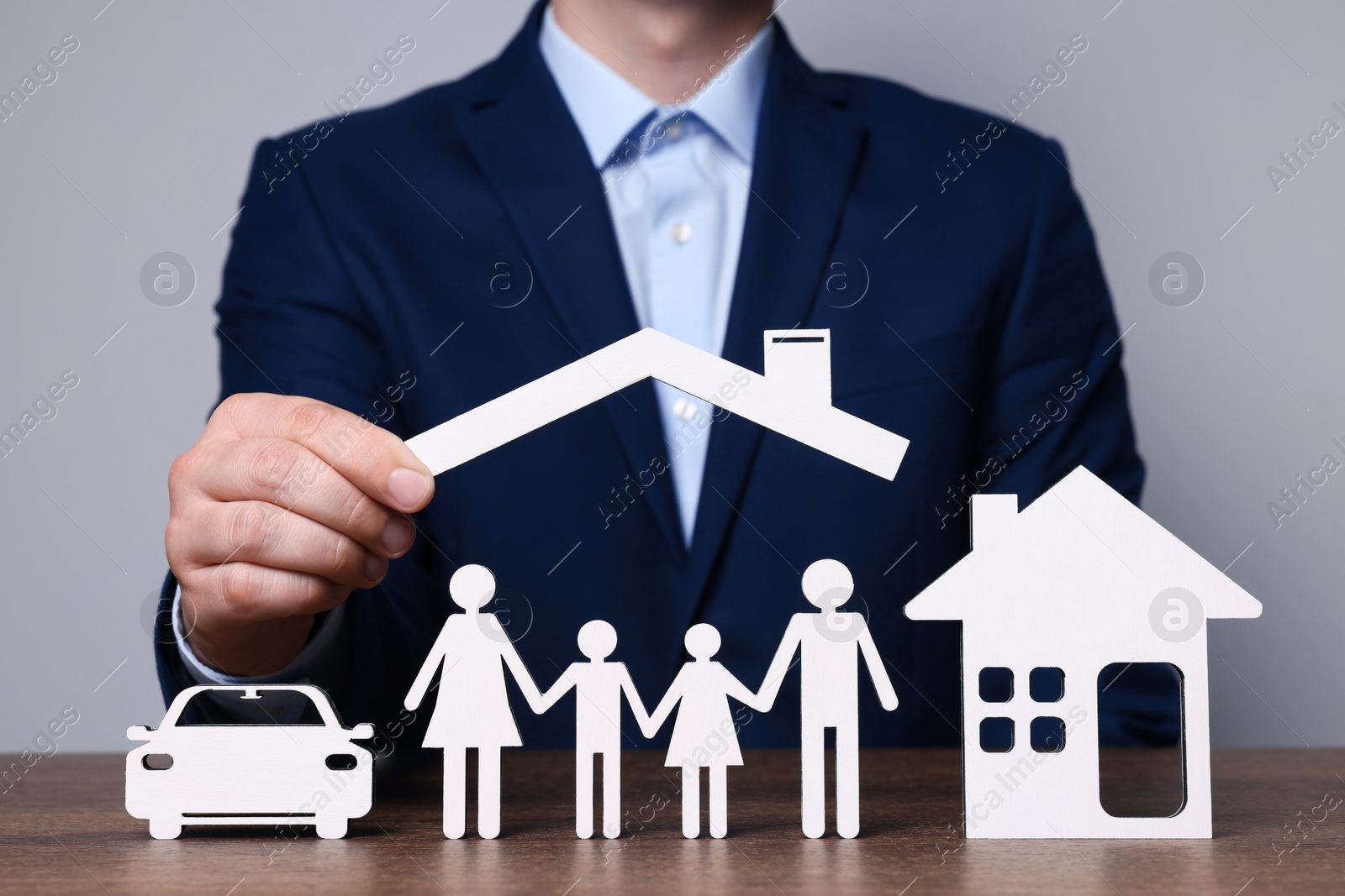 Photo of Man holding figure of roof above family at wooden table. closeup. Insurance concept