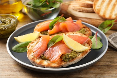 Photo of Delicious bruschettas with salmon and pesto sauce on wooden table, closeup