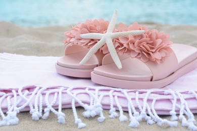Photo of Blanket with stylish slippers and starfish on sand near sea, closeup. Beach accessories