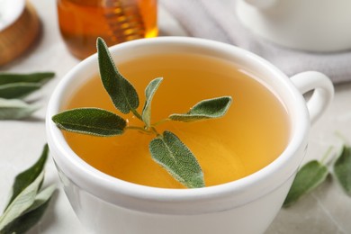 Photo of Cup of aromatic sage tea with fresh leaves on table, closeup