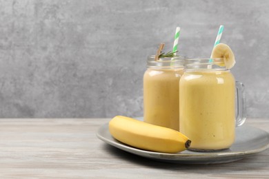 Tasty banana smoothie and fresh fruit on white wooden table. Space for text