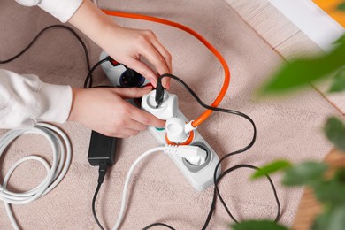 Photo of Woman putting plug into power strip on white floor indoors, closeup