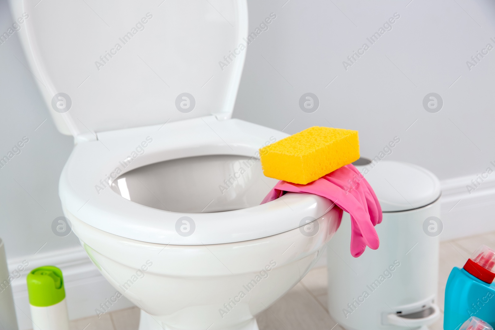 Photo of Ceramic toilet bowl, bottles of detergent and cleaning supplies in modern bathroom