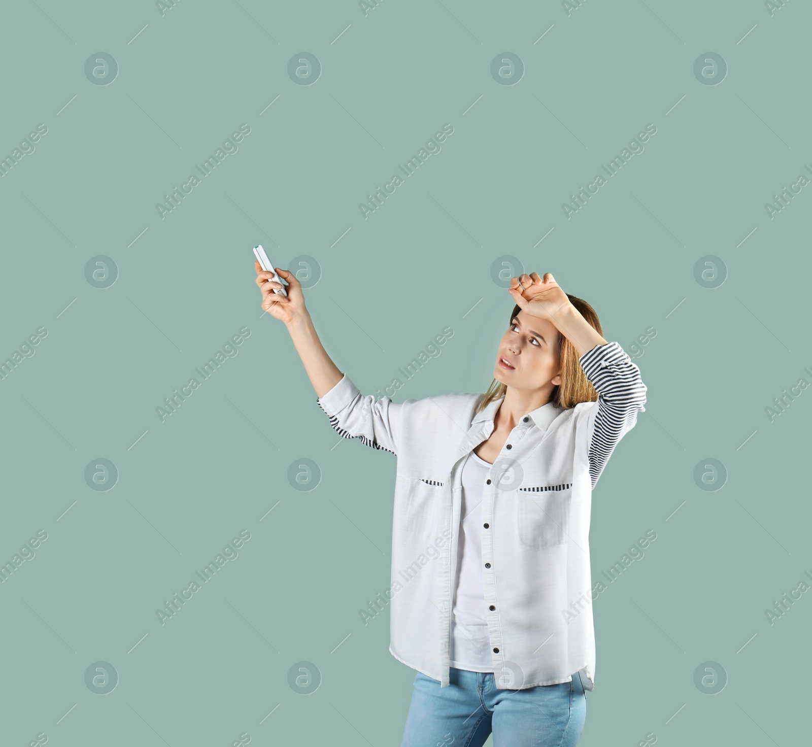 Photo of Woman with air conditioner remote suffering from heat on color background