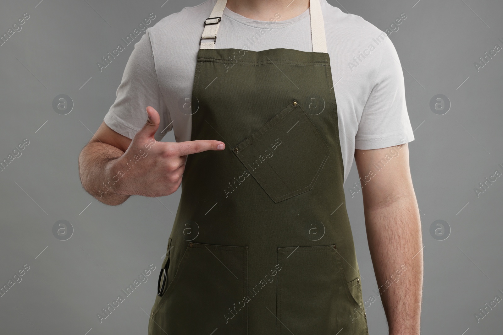 Photo of Man pointing at kitchen apron on grey background, closeup. Mockup for design