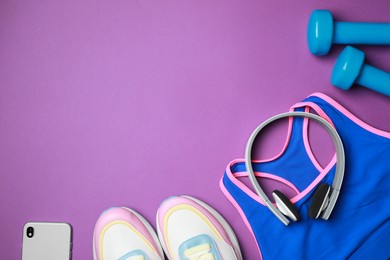 Photo of Stylish sportswear, dumbbells, smartphone and headphones on purple background, flat lay. Space for text