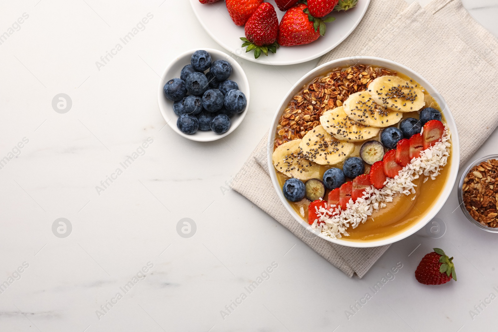 Photo of Delicious smoothie bowl with fresh berries, banana, coconut flakes and granola on white marble table, flat lay. Space for text