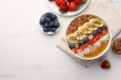 Delicious smoothie bowl with fresh berries, banana, coconut flakes and granola on white marble table, flat lay. Space for text
