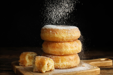 Photo of Delicious donuts with powdered sugar on wooden table