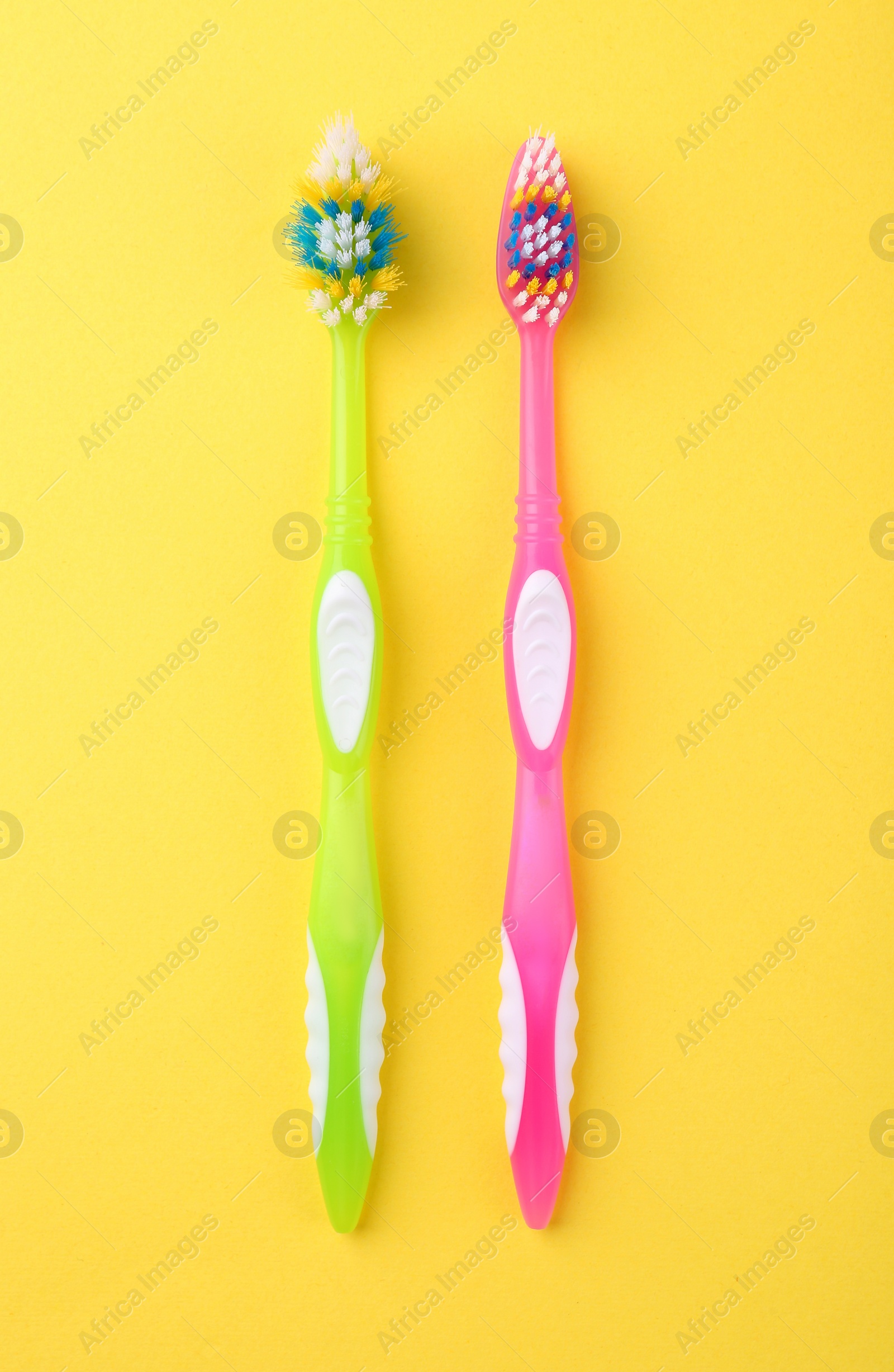 Photo of Colorful plastic toothbrushes on yellow background, flat lay