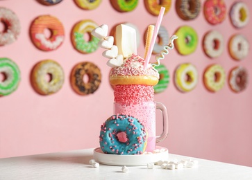 Photo of Mason jar of tasty milk shake with sweets on table in cafe