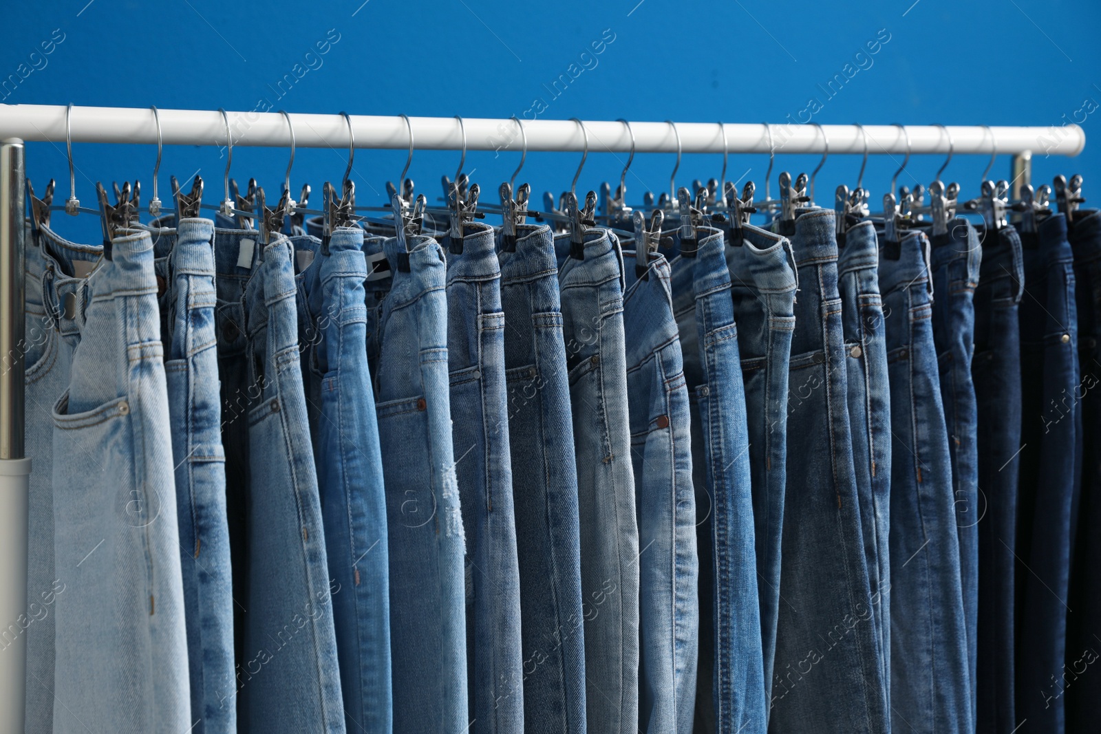 Photo of Rack with stylish jeans on blue background, closeup