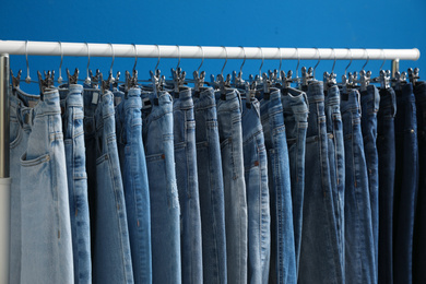 Rack with stylish jeans on blue background, closeup
