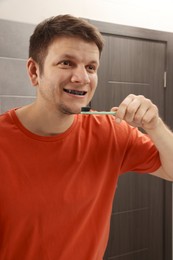 Photo of Man brushing teeth with charcoal toothpaste in bathroom