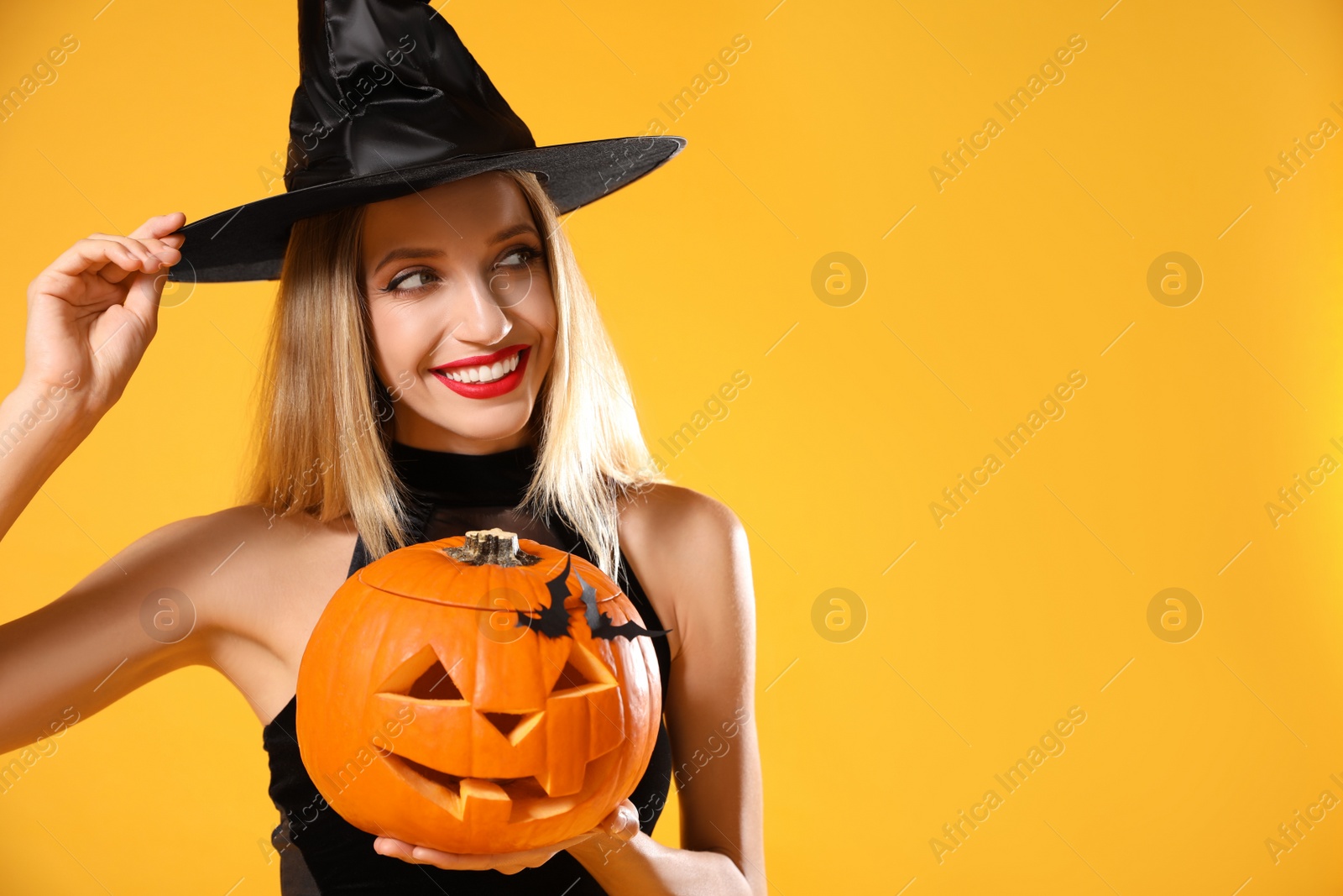 Photo of Beautiful woman in witch costume with jack o'lantern on yellow background, space for text. Halloween party