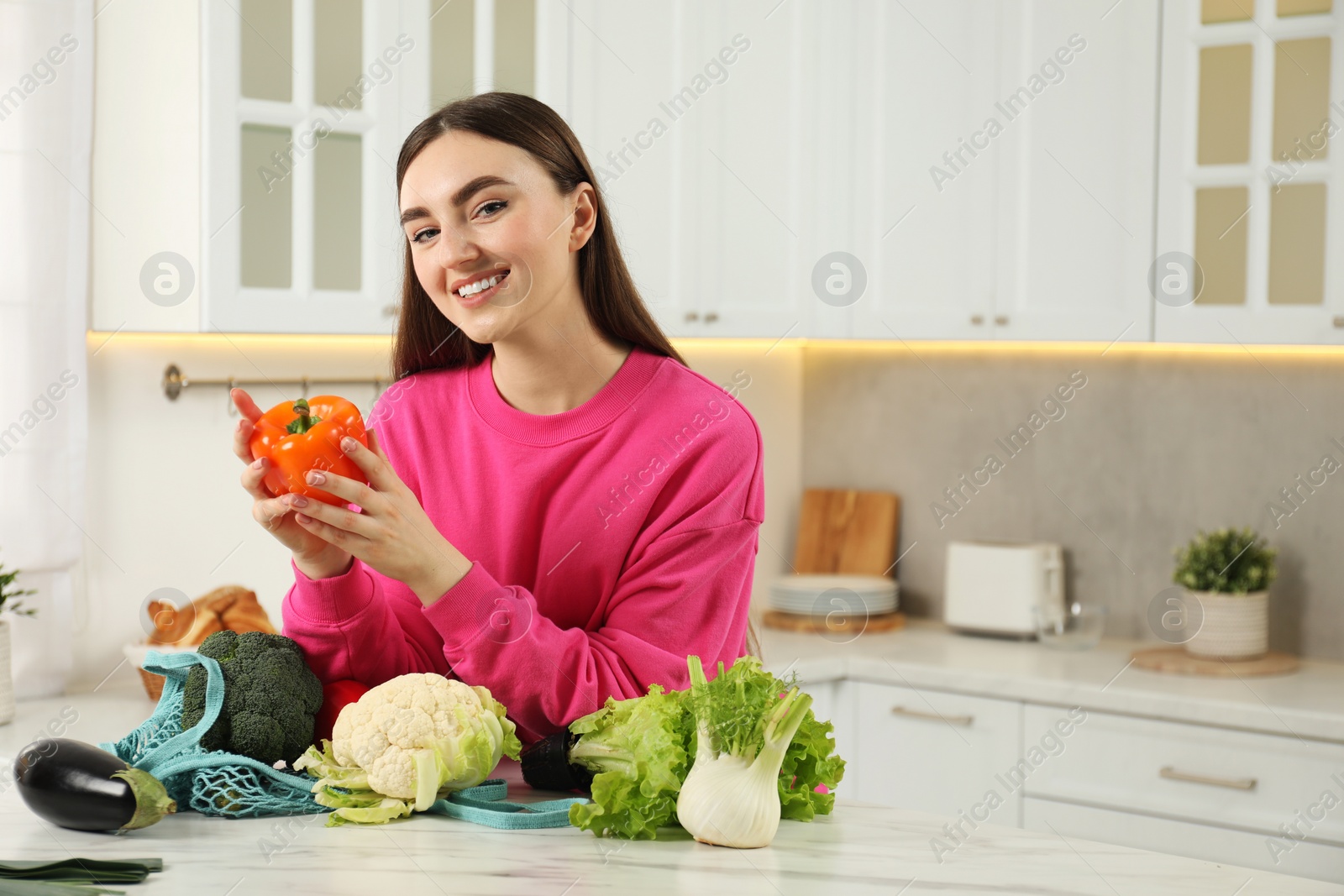 Photo of Woman with pepper and string bag of vegetables at light marble table in kitchen
