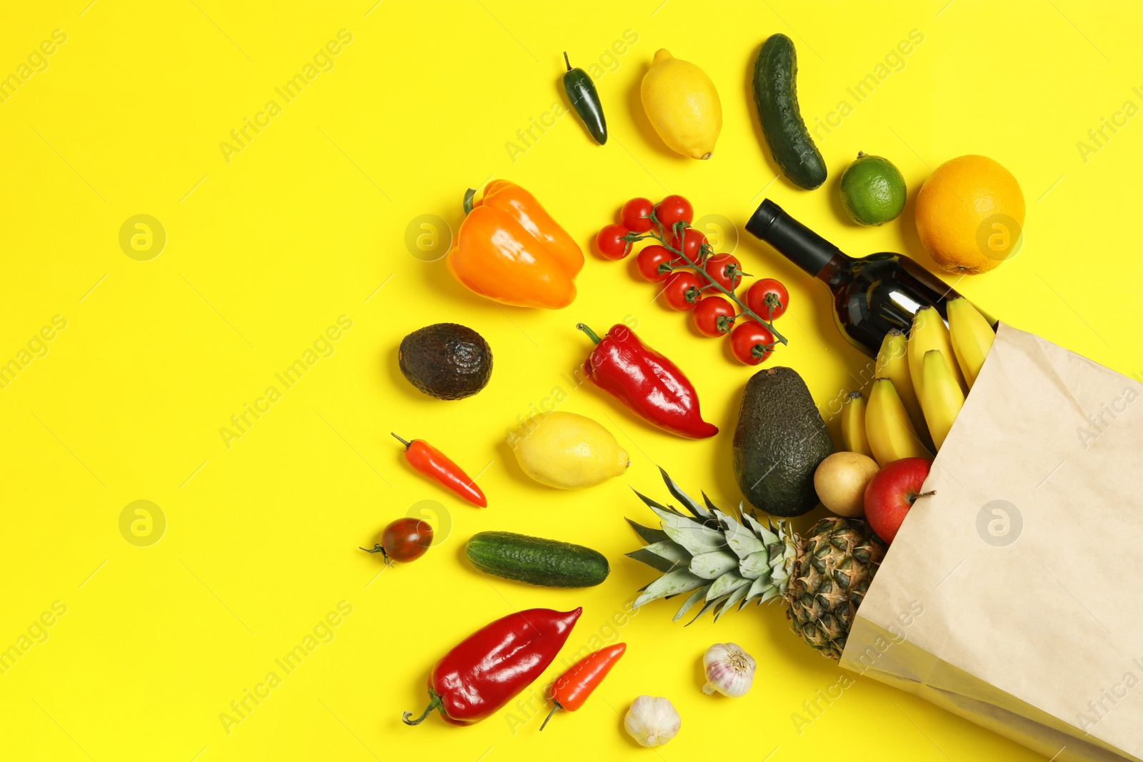 Photo of Shopping paper bag with different groceries on yellow background, flat lay. Space for text