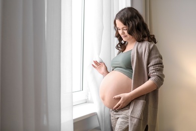 Young pregnant woman near window at home