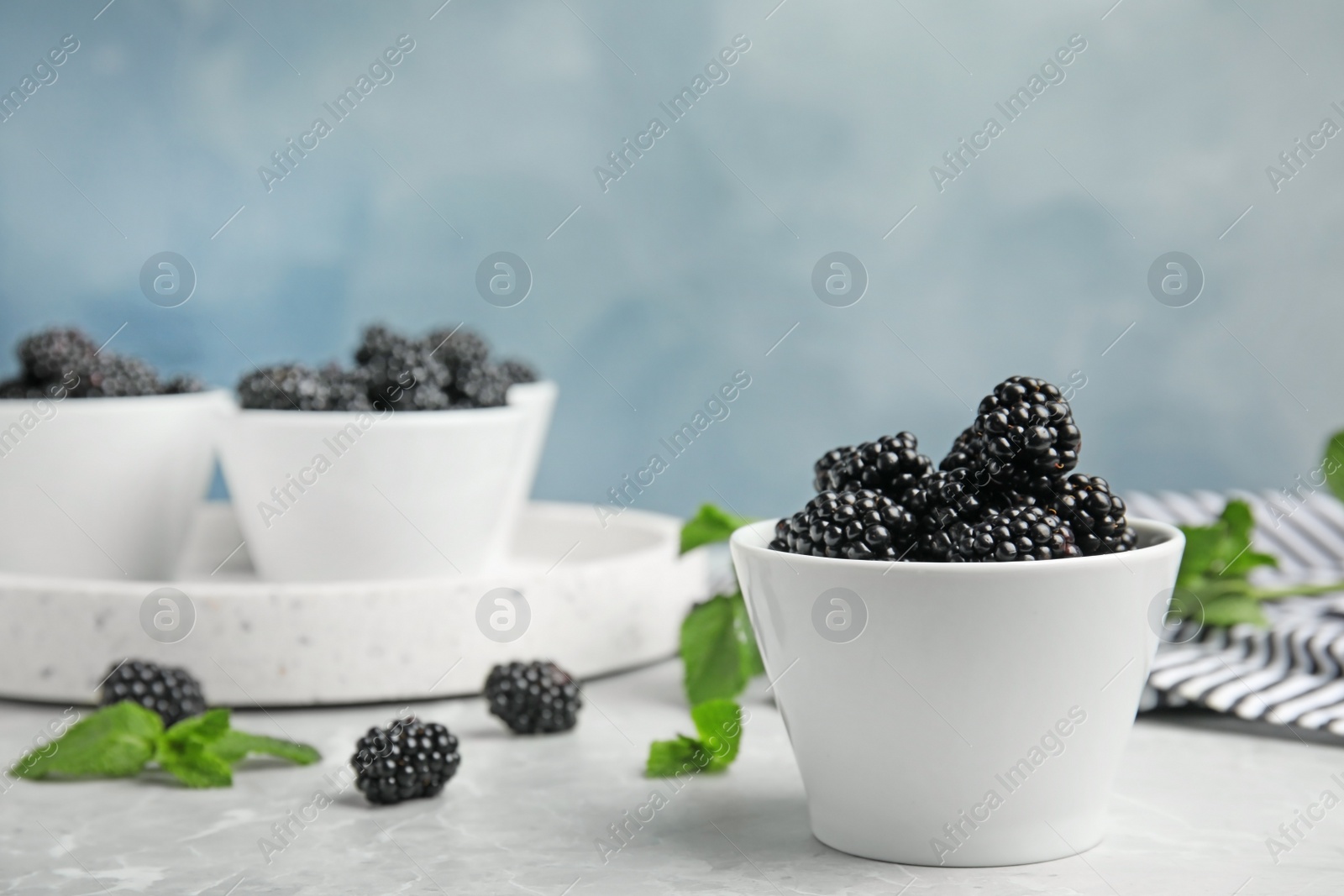 Photo of Bowls of tasty blackberries on grey marble table. Space for text