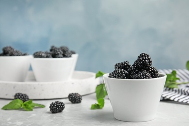 Bowls of tasty blackberries on grey marble table. Space for text