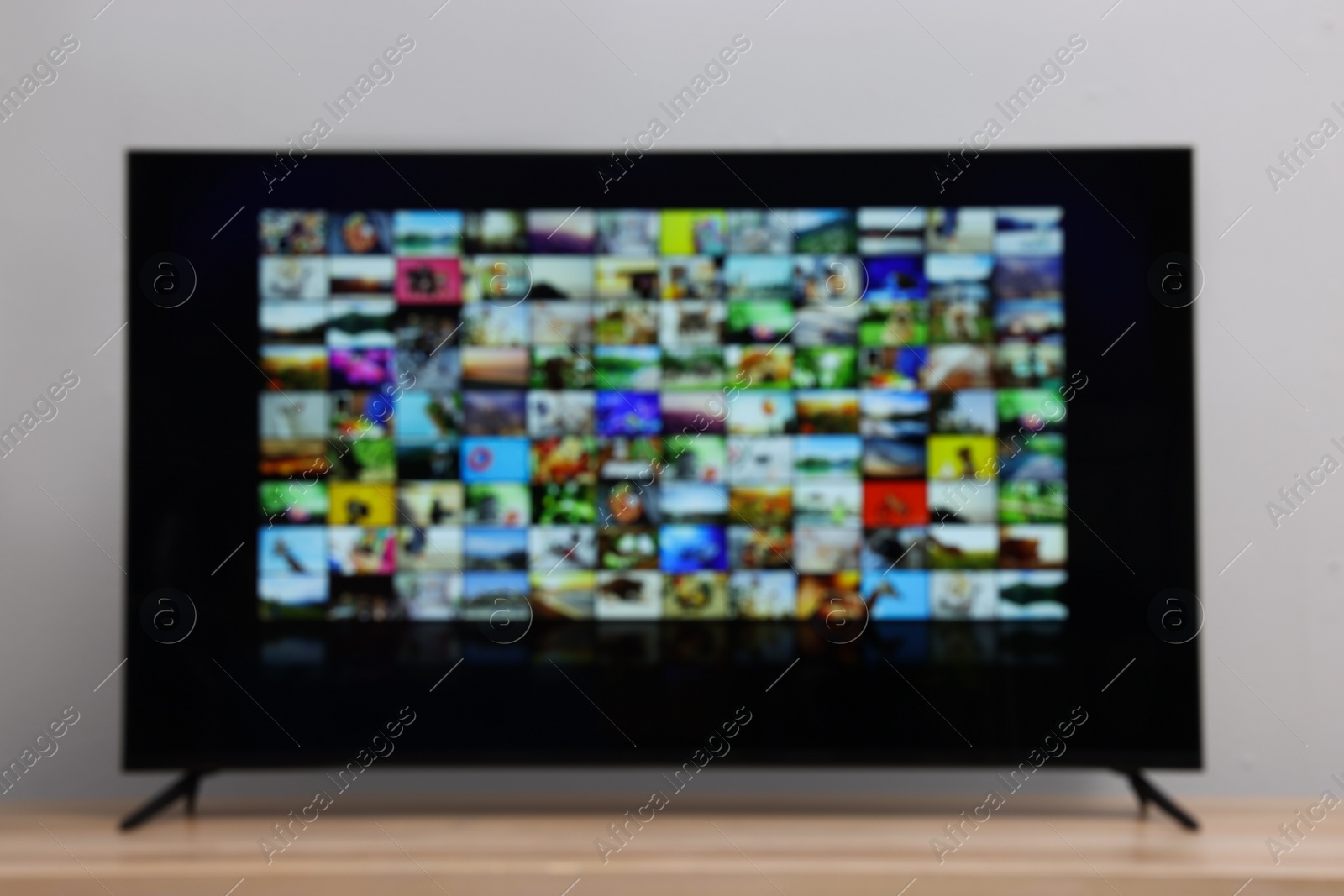 Photo of Blurred view of modern TV set with streaming video on screen near white wall indoors