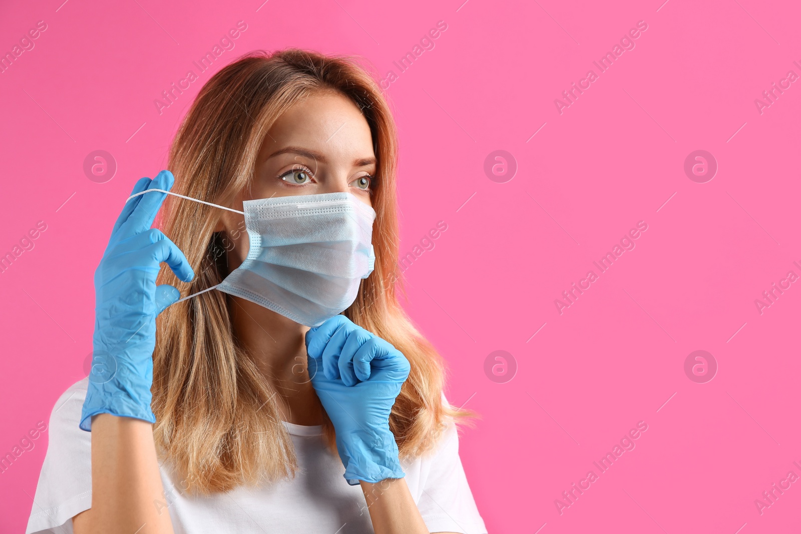 Photo of Woman in medical gloves putting on protective face mask against pink background. Space for text