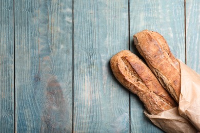 Photo of Tasty buckwheat baguettes in package on light blue wooden table, top view. Space for text