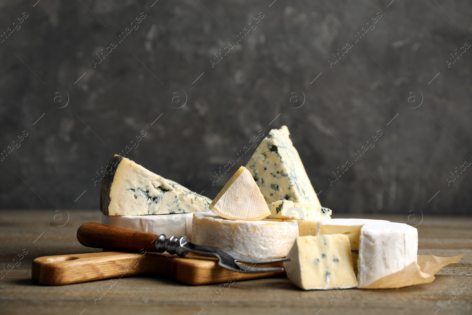 Photo of Different sorts of cheese and fork on wooden table against grey background