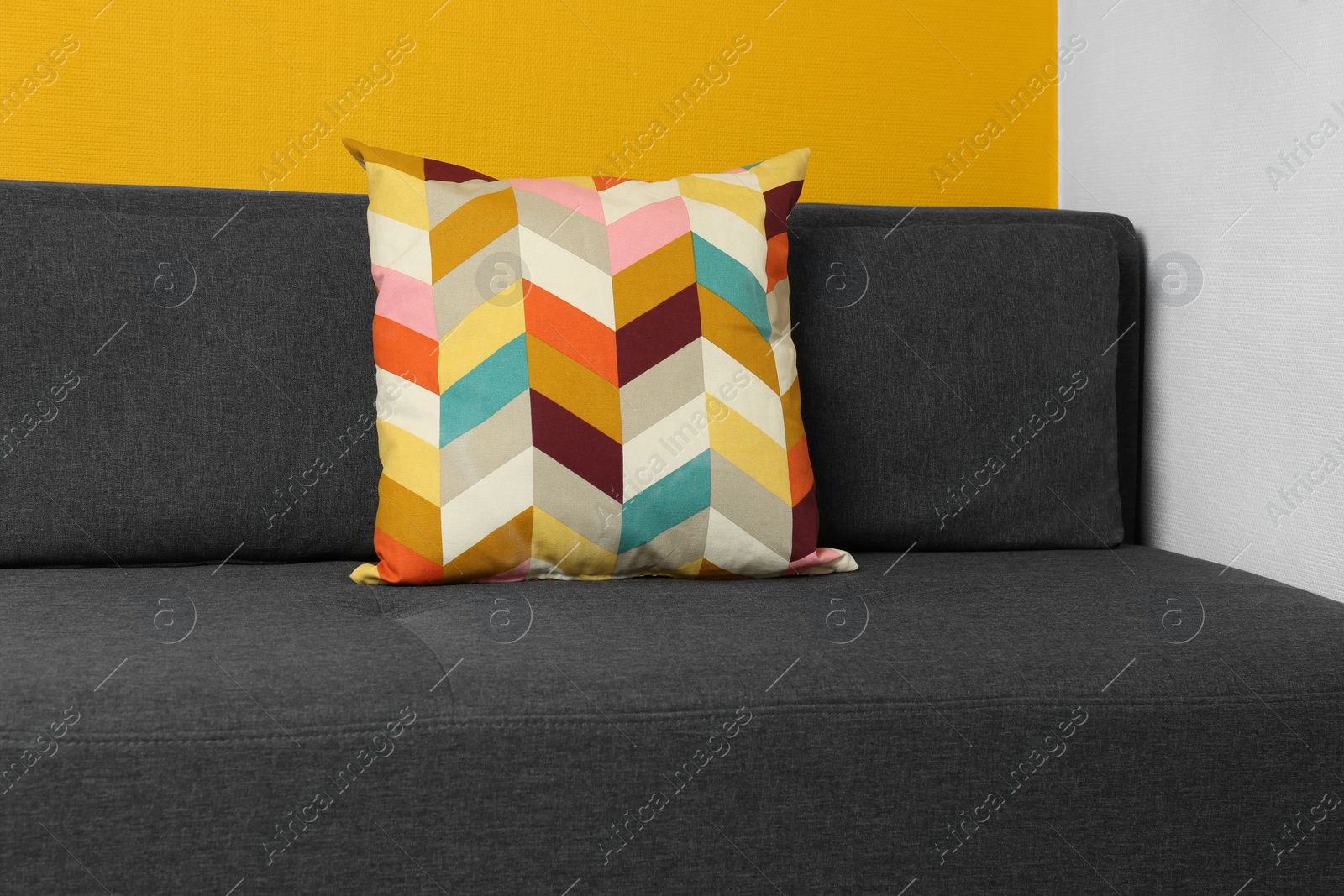 Photo of Stylish grey sofa with bright cushion in room