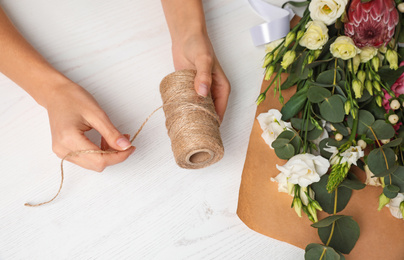 Photo of Florist making beautiful bouquet at white wooden table, top view