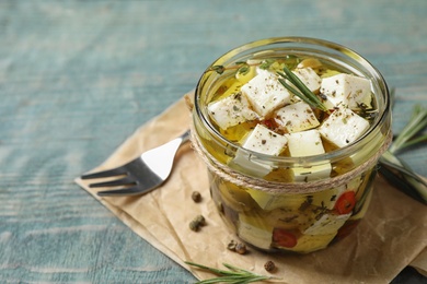 Composition with pickled feta cheese in jar on blue wooden table, space for text